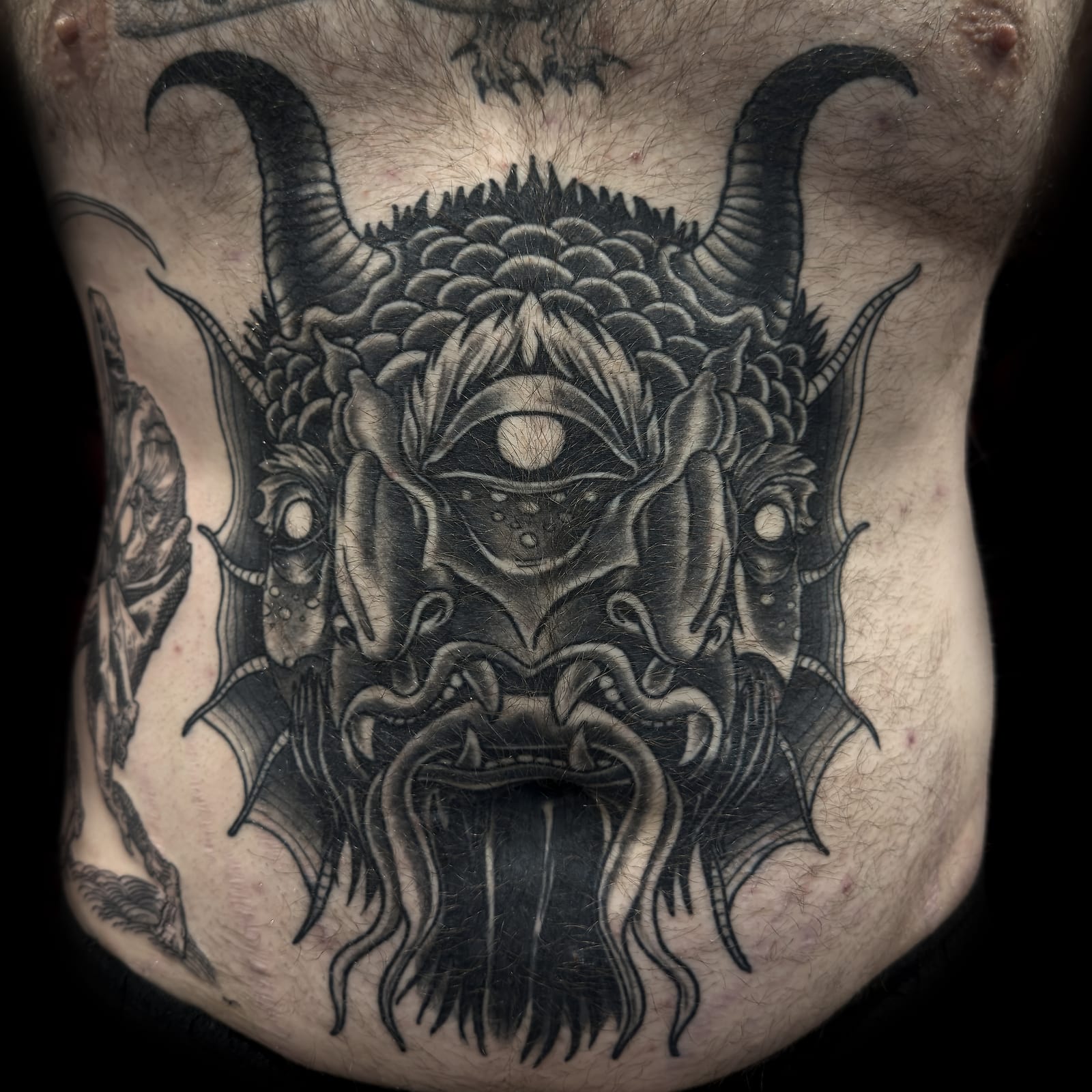 Healed blackwork demon tattoo covering the stomach.