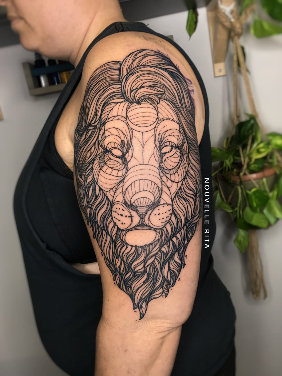Large fine-line lion tattoo with flowing geometric linework on an upper arm.