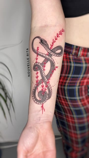 Two fine-line snakes entwined with red botanical stems on an inner forearm.