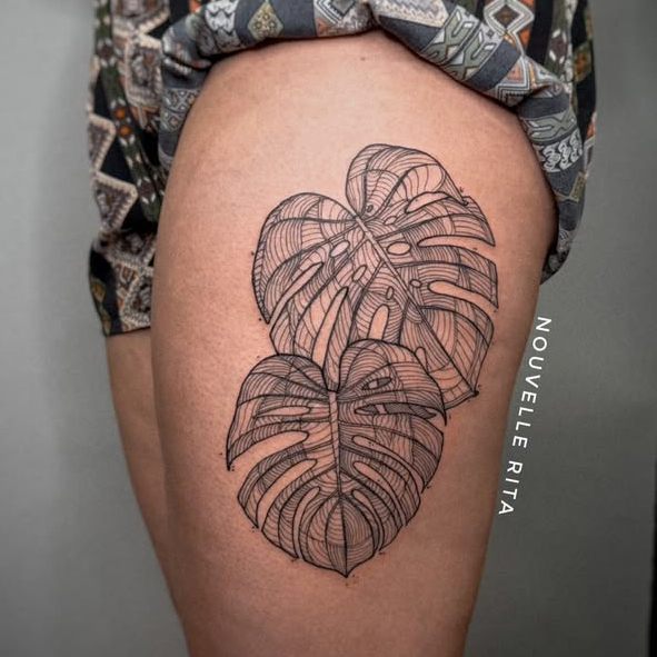 Fine-line botanical tattoo of two monstera leaves on a thigh.