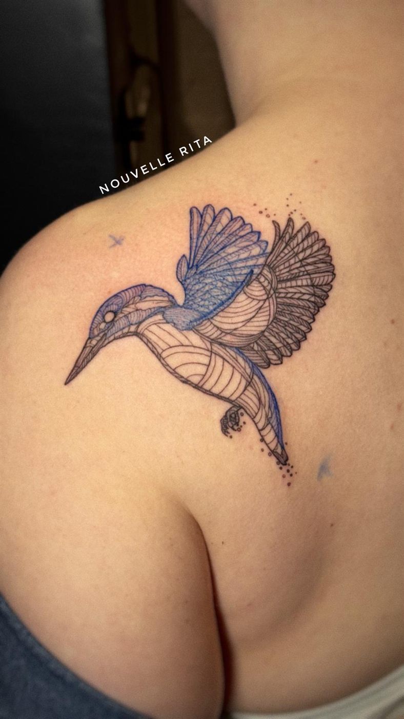Fine-line wildlife tattoo of a kingfisher in flight, with blue detailing, on a shoulder.